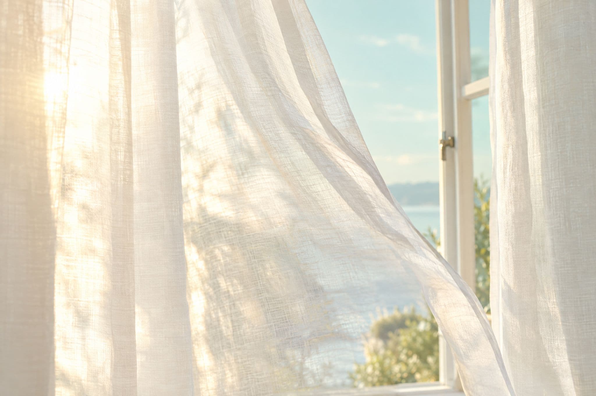 Sheer linen curtains glowing in a sunlit open window